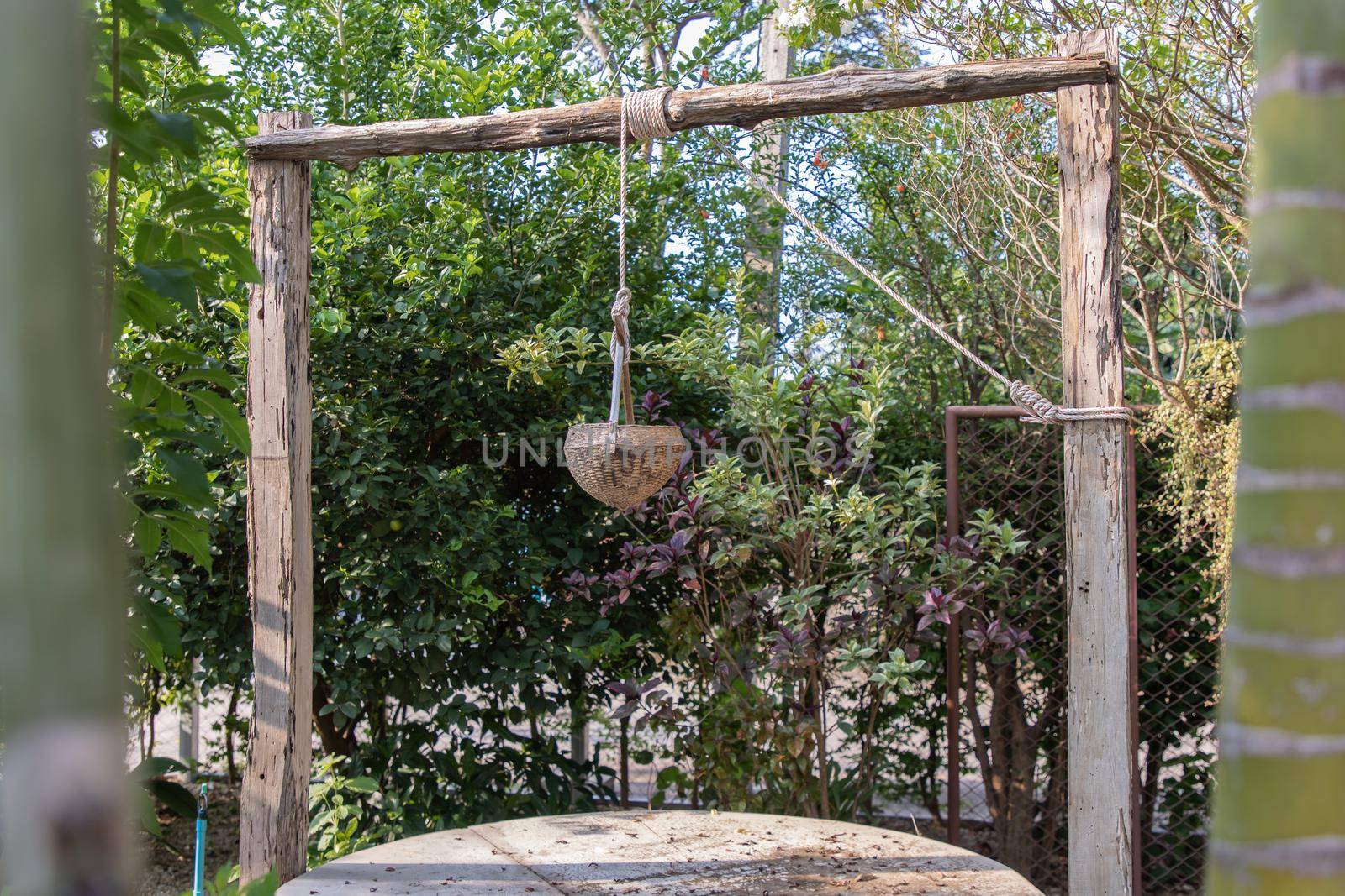 Old wooden well (water source) in traditional village folk style. At time of scooping the rope, put wooden water scoop into the pond to draw water.
