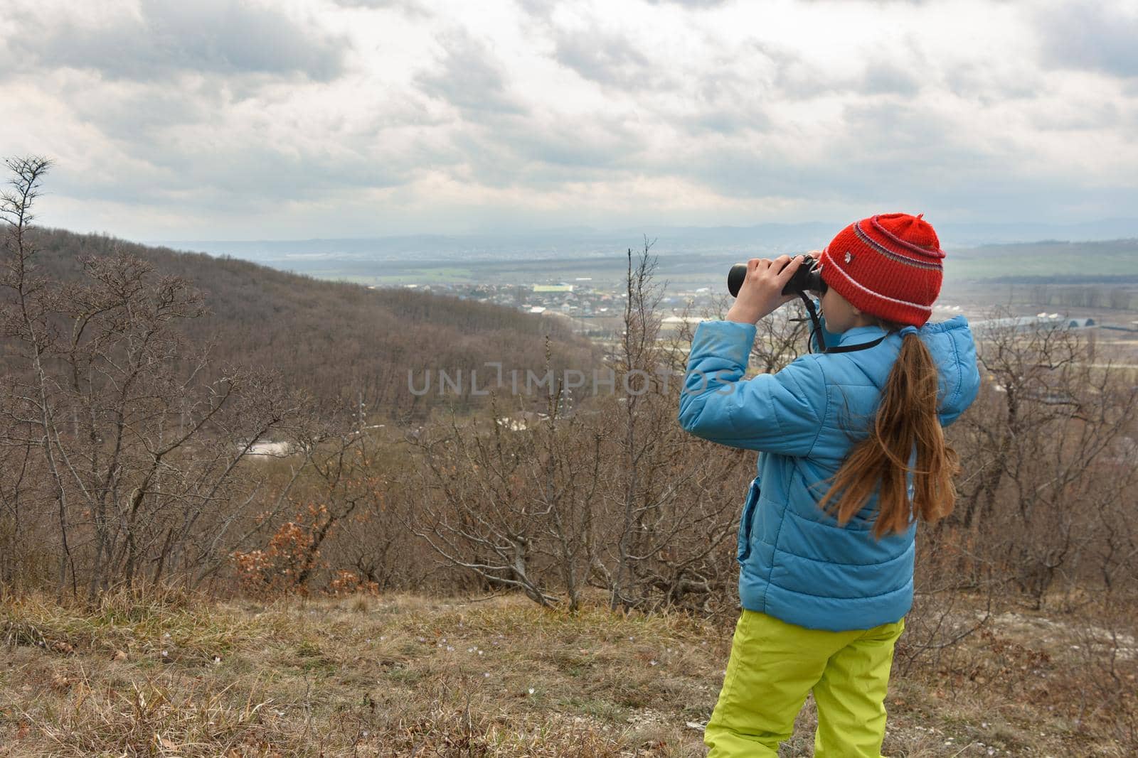 A girl examines a mountain landscape through binoculars, view from the back by Madhourse