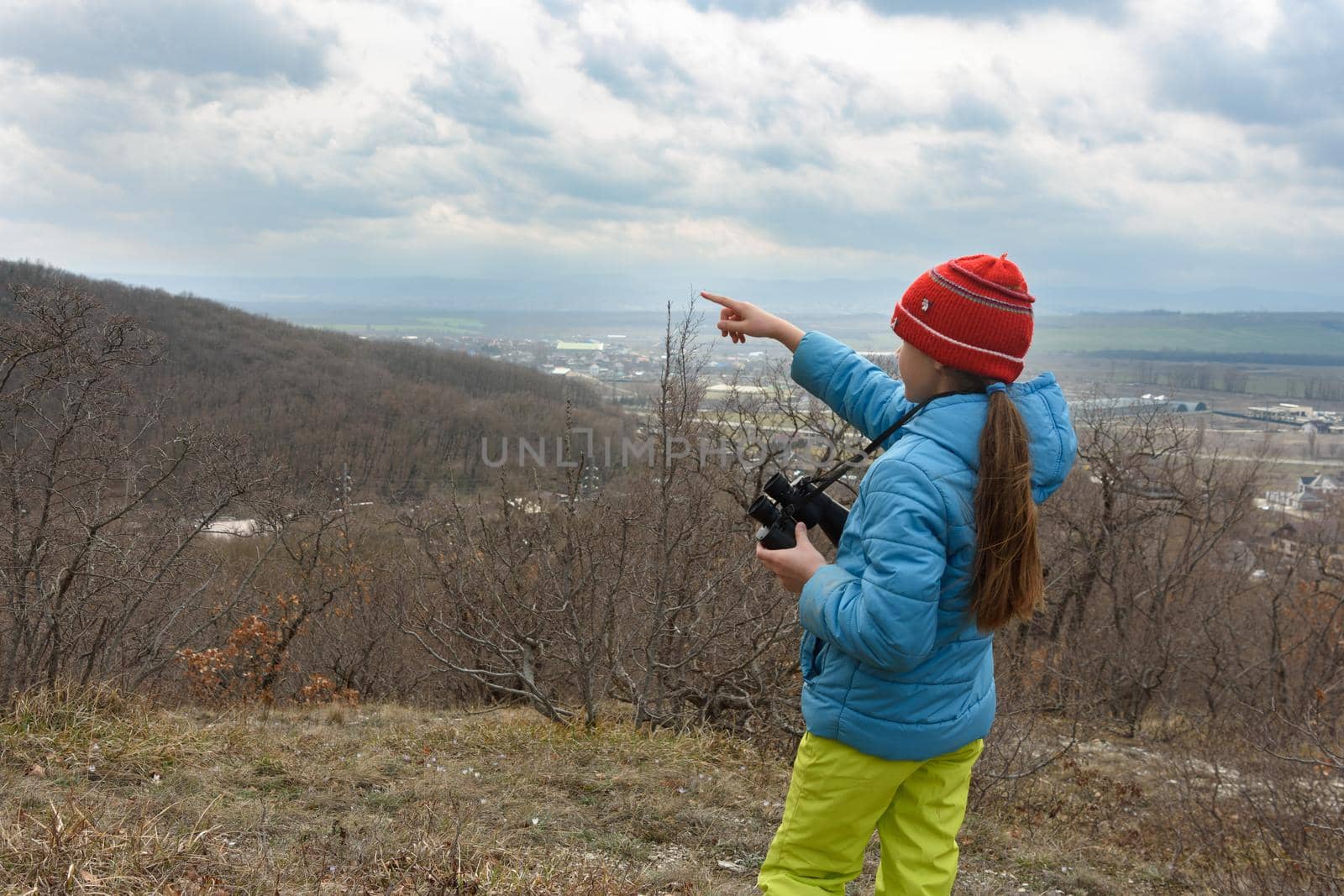 The girl saw something through binoculars, looking at the mountains and points there with her finger