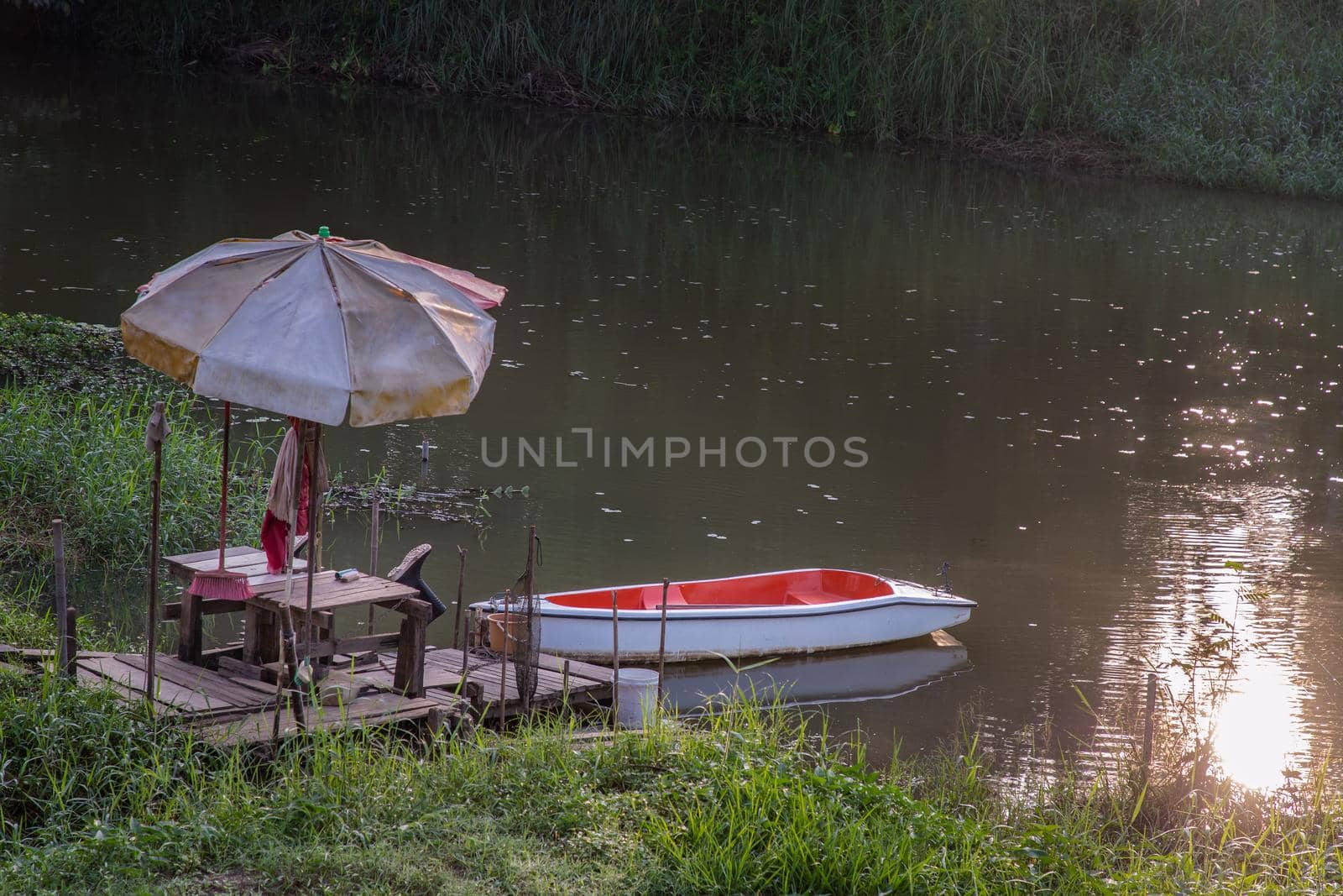 Rowboat moored to a rustic jetty along the canal amongst grass and water in a scenic rural landscape. Selective focus.