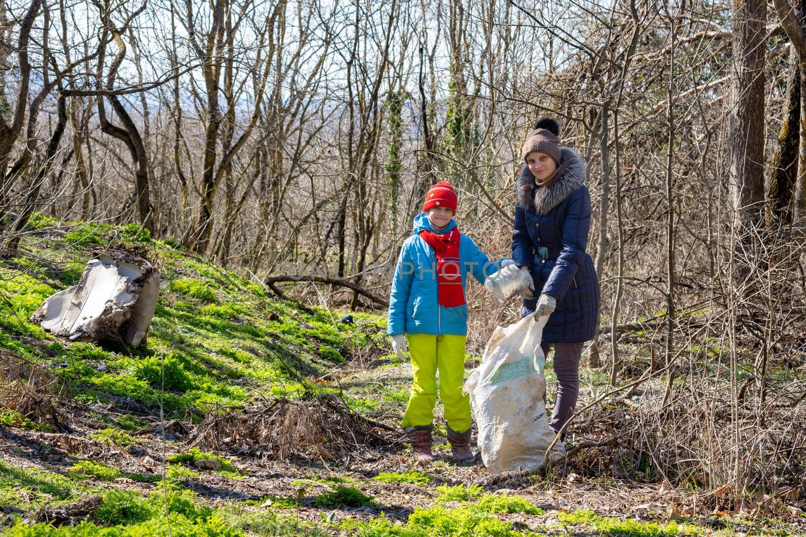A girl and her daughter collect garbage in the forest in early spring, they looked into the frame