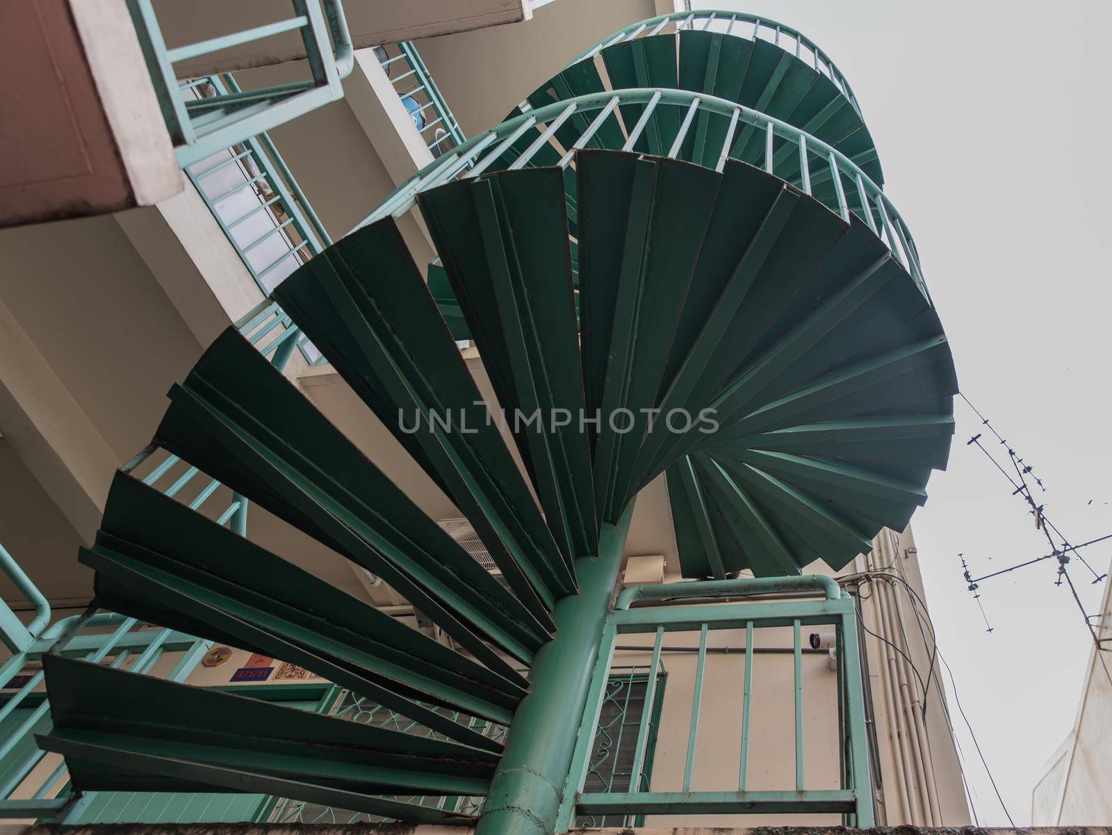Green spiral staircase pattern view from below. Spiral stairs circle in courtyard architecture. Outdoor ladder decoration interior. Selective focus.