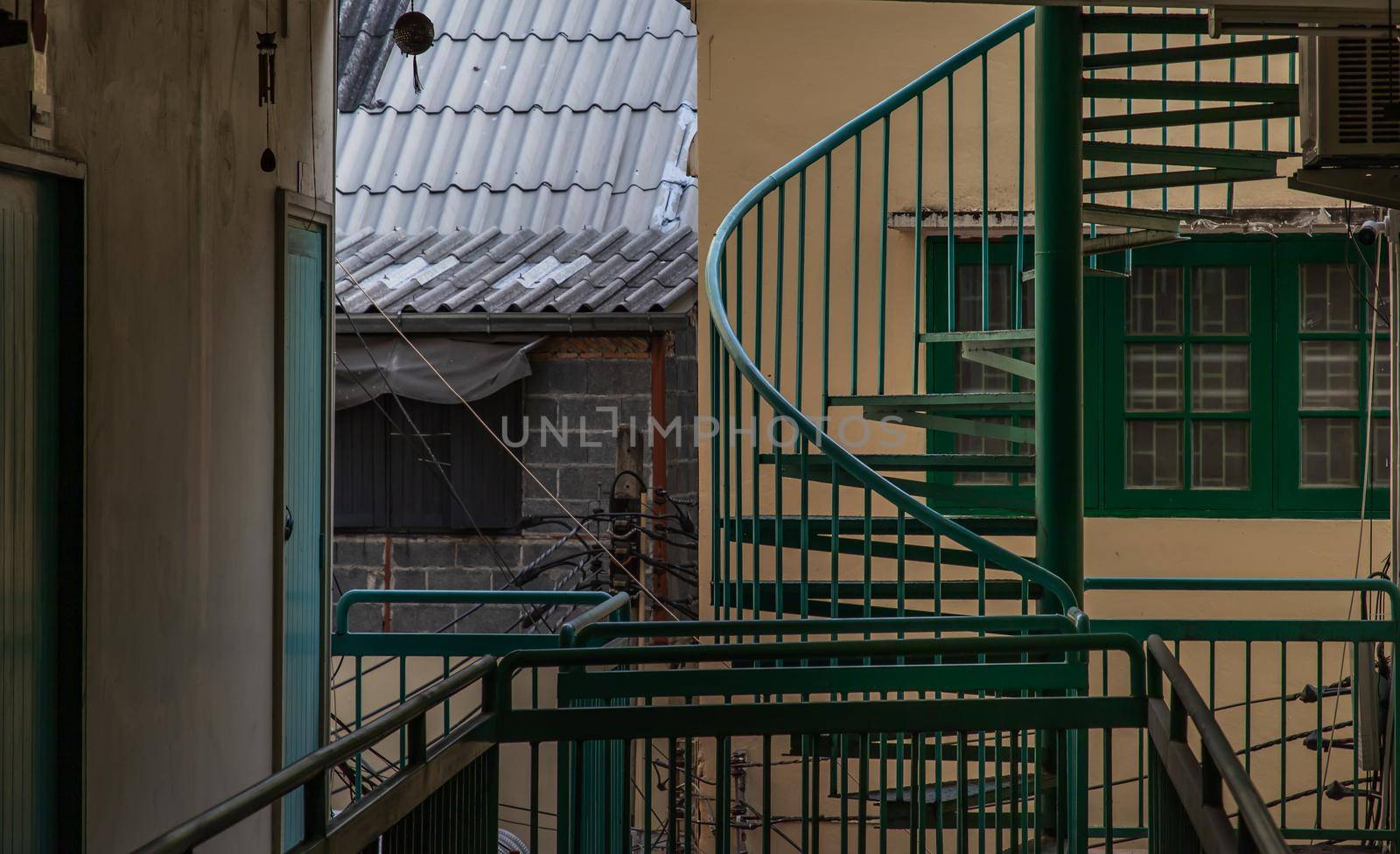 Bangkok, Thailand - 25 Jan 2020 : Green spiral staircase pattern in old apartment. Spiral stairs circle in courtyard architecture. Outdoor ladder decoration interior. Selective focus.