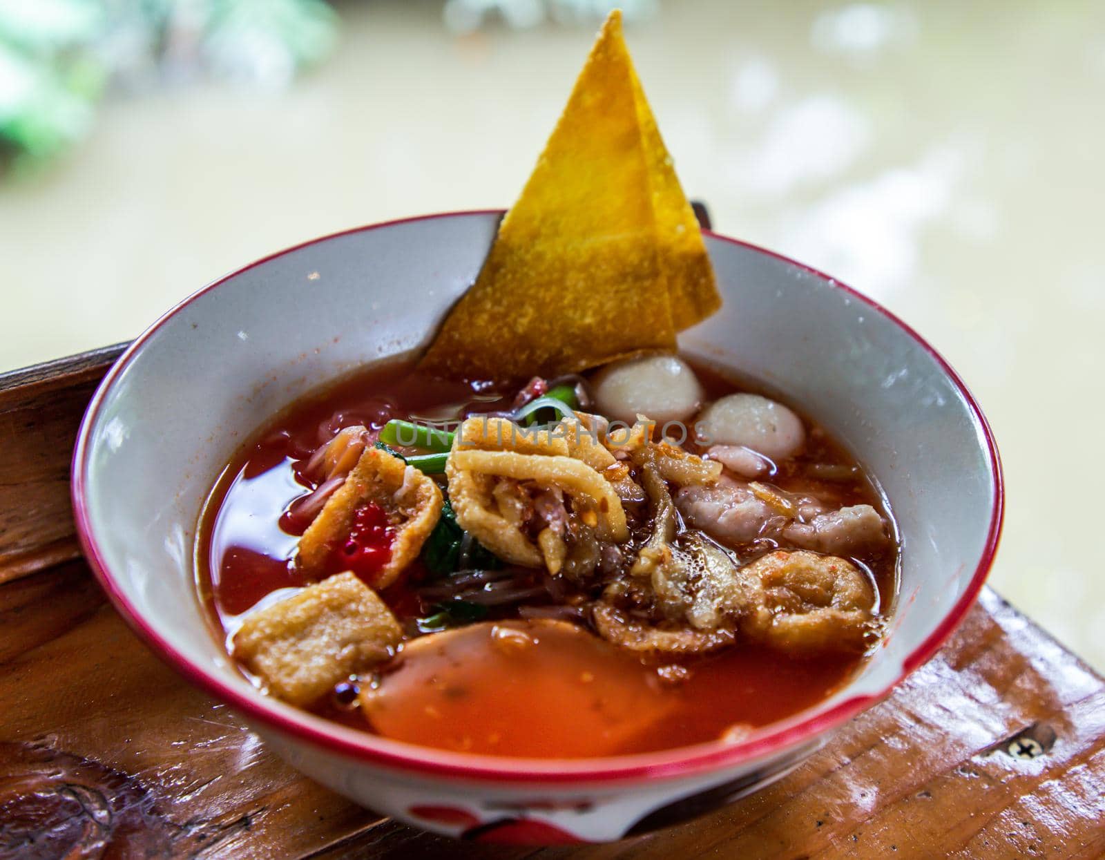 Yentafo Thai Noodle with pink soup in ceramic bowl on wooden table. Copy space, Selective focus.