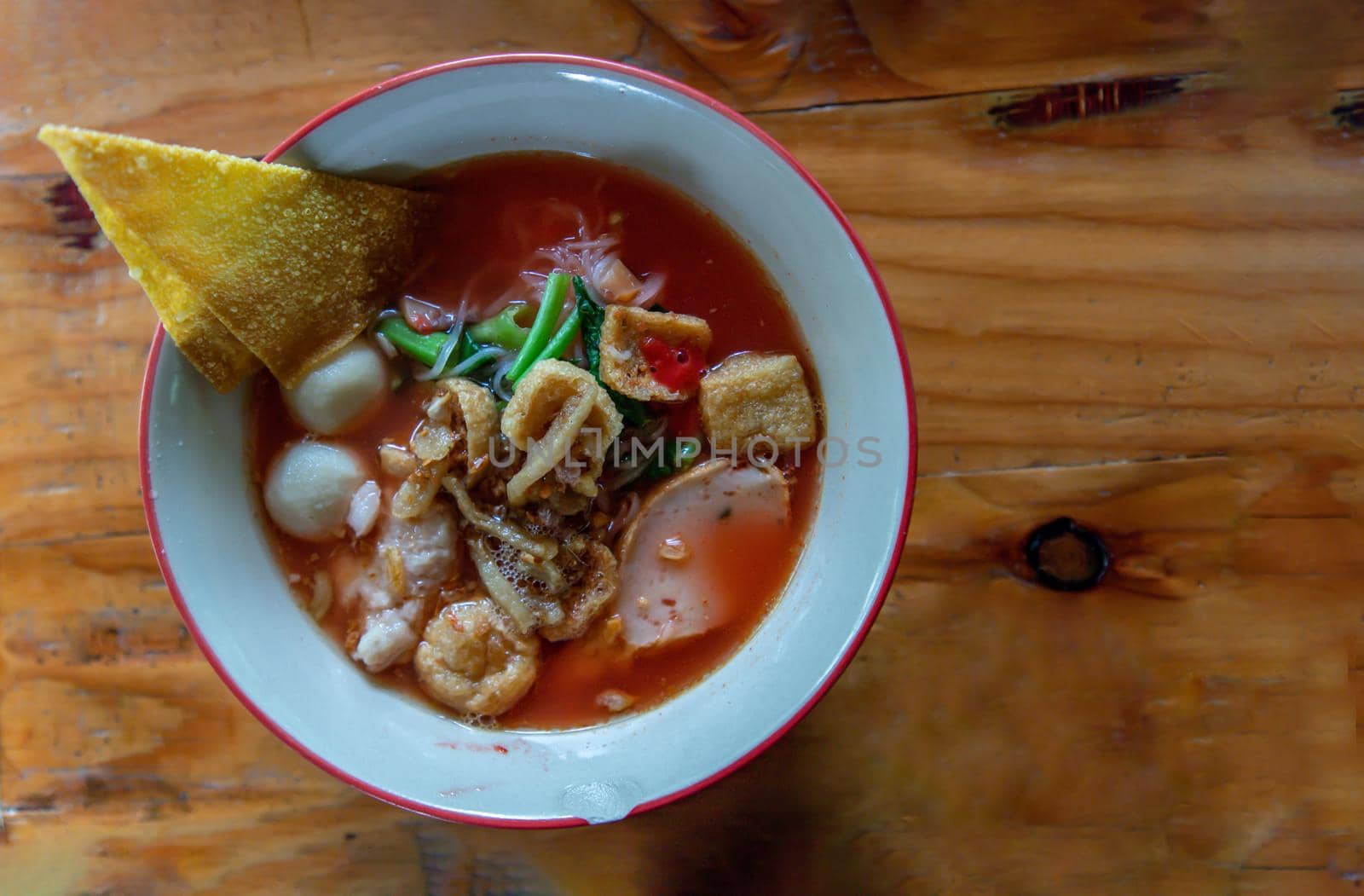 Yentafo Thai Noodle with pink soup in ceramic bowl on wooden table. Top view, Copy space, Selective focus.