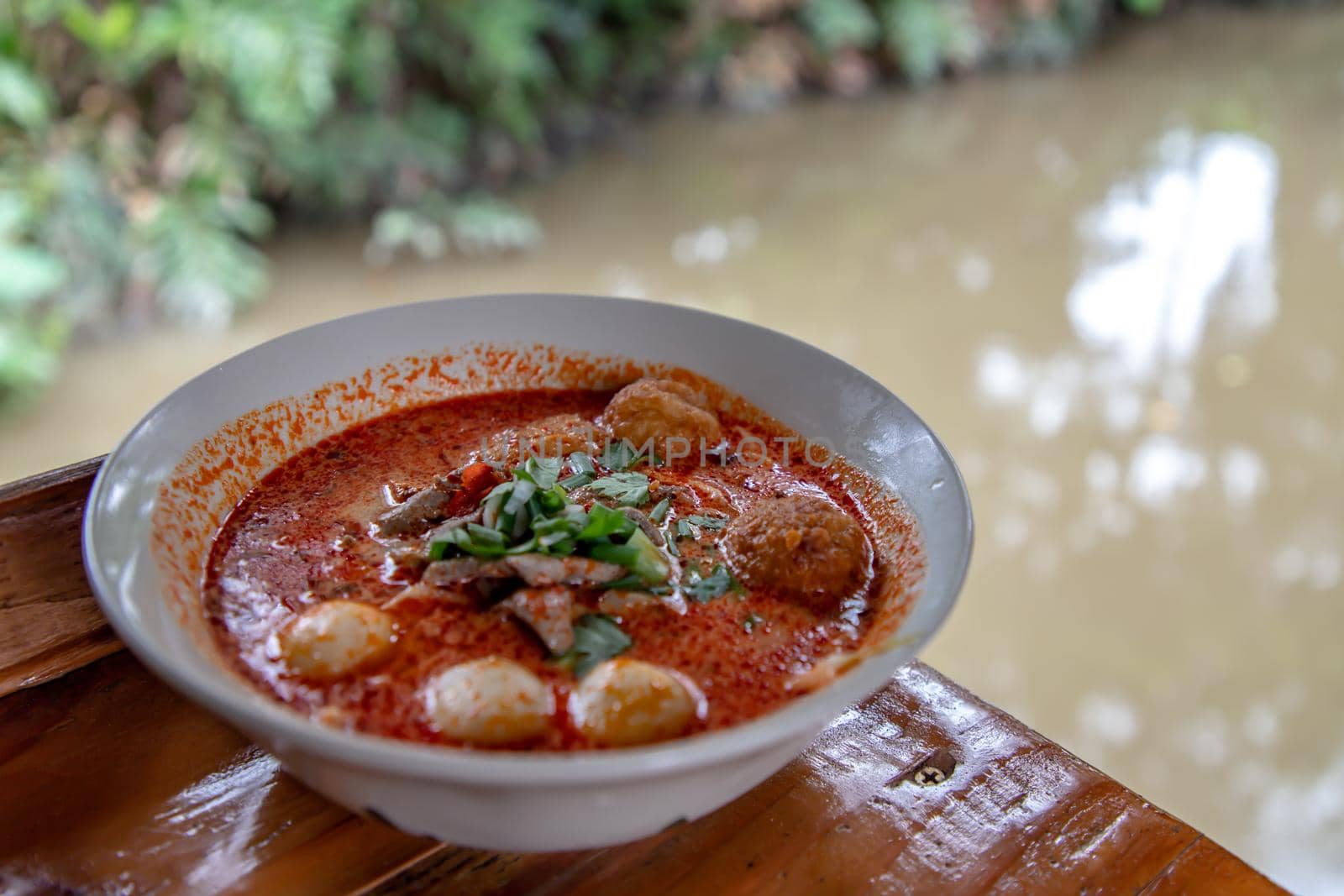 Spicy tom yum pork soup or Spicy lemongrass flavored soup with fish balls in ceramic bowl on wooden table. Copy space, Selective focus.