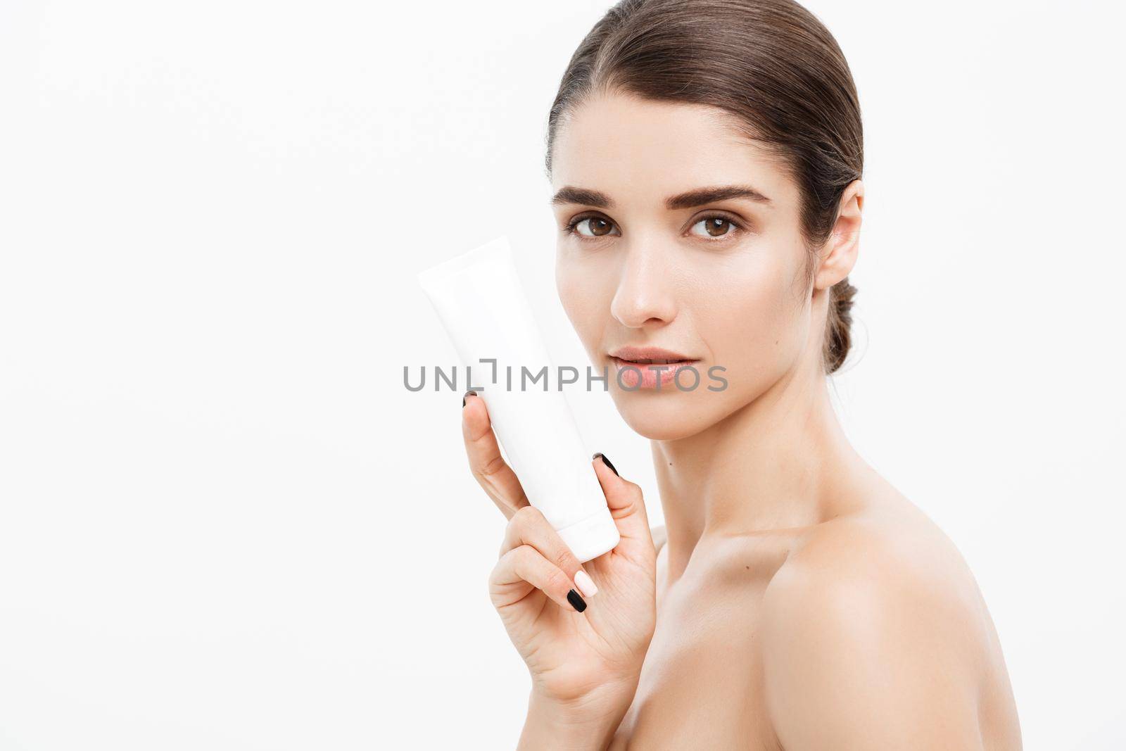 Beauty Youth Skin Care Concept - Beautiful Caucasian Woman Face Portrait holding and presenting cream tube product. Beautiful Spa model Girl with Perfect Fresh Clean Skin over white background