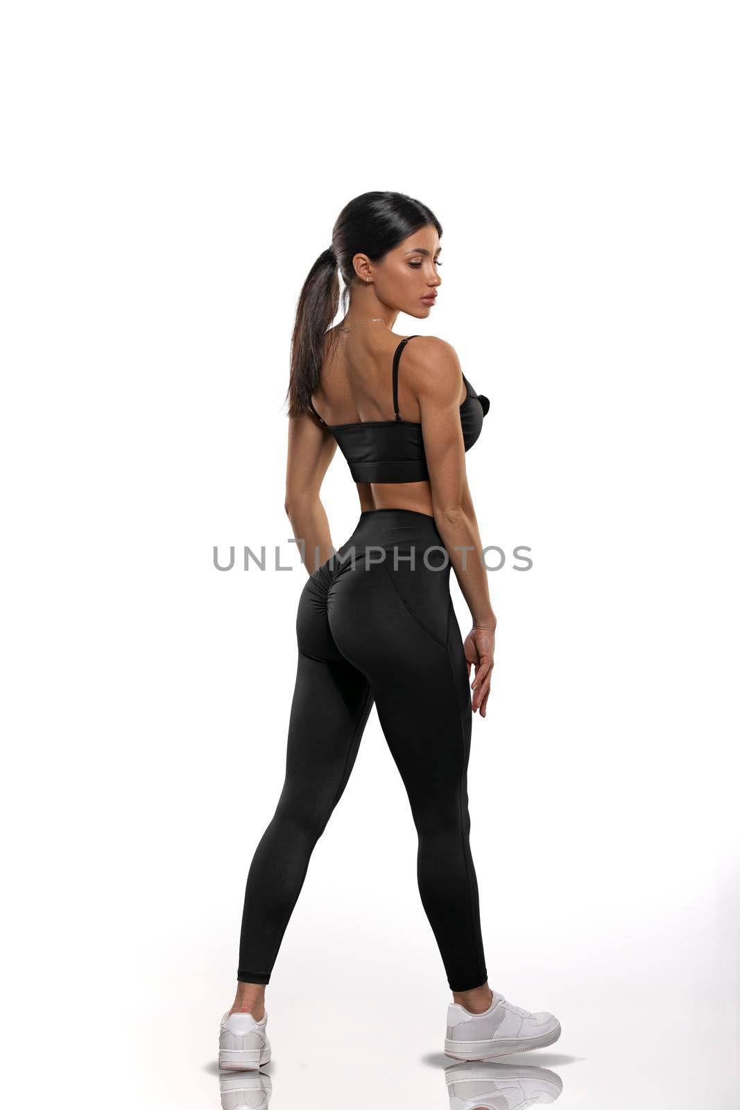brunette girl in black leggings and a top stay back on a white background