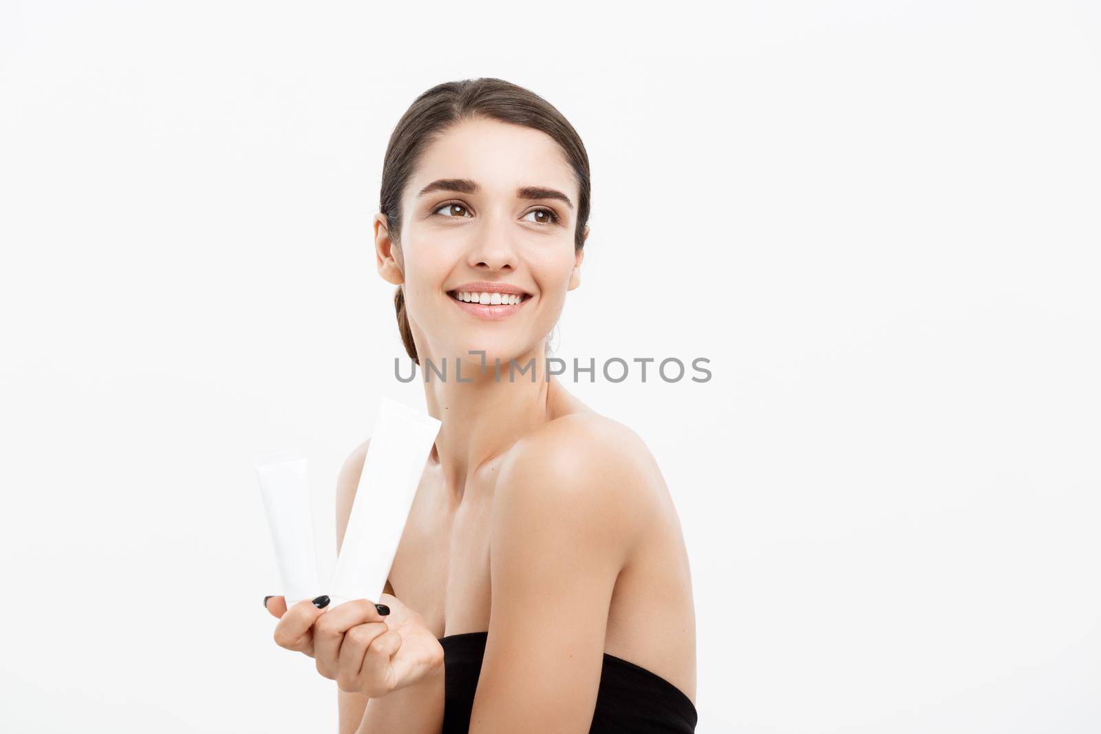 Beauty Youth Skin Care Concept - Beautiful Caucasian Woman Face Portrait holding and presenting cream tube product. Beautiful Spa model Girl with Perfect Fresh Clean Skin over white background
