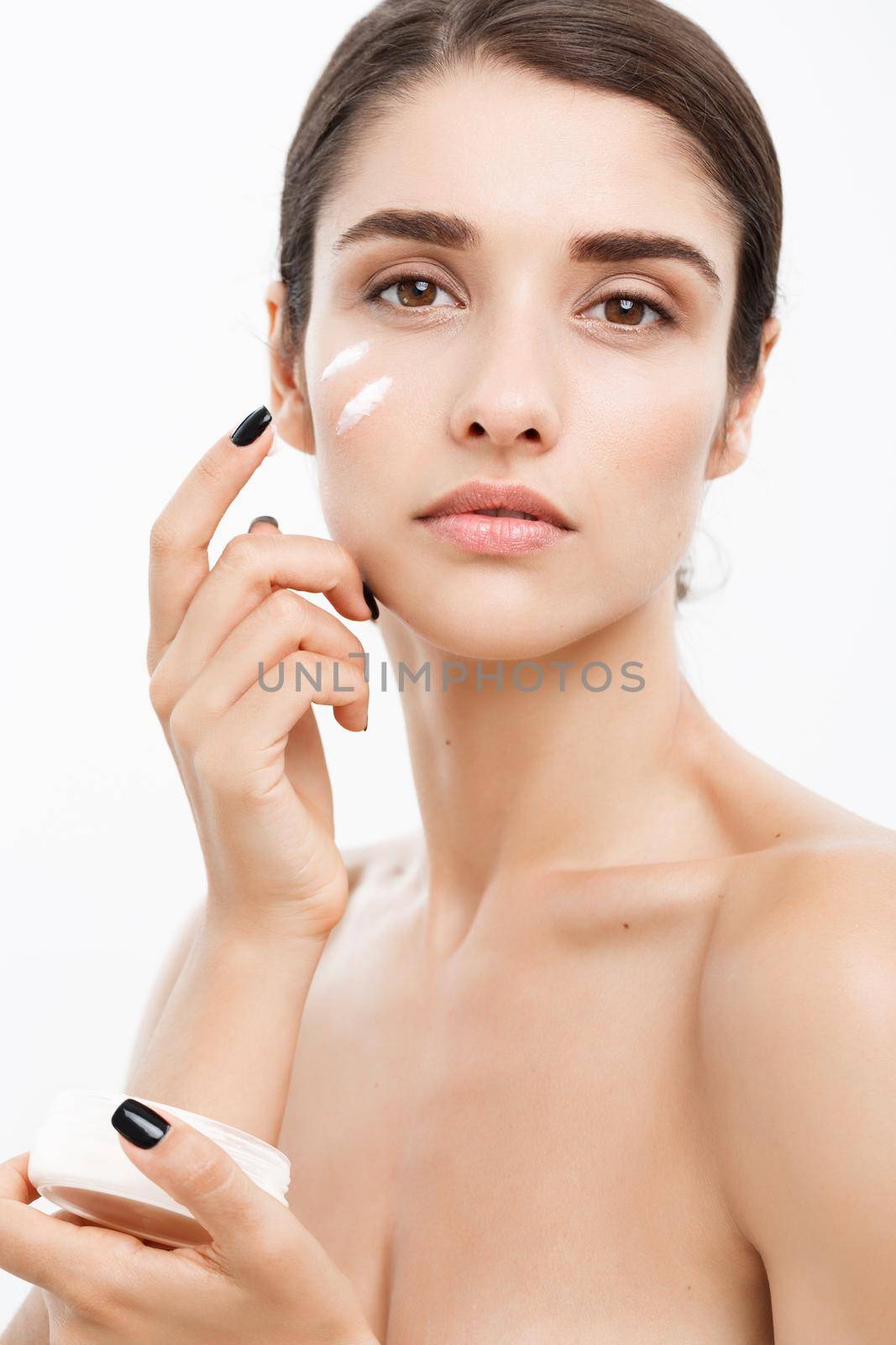 Beauty Youth Skin Care Concept - Close up Beautiful Caucasian Woman Face Portrait applying some cream to her face. Beautiful Spa model Girl with Perfect Fresh Clean Skin over white background