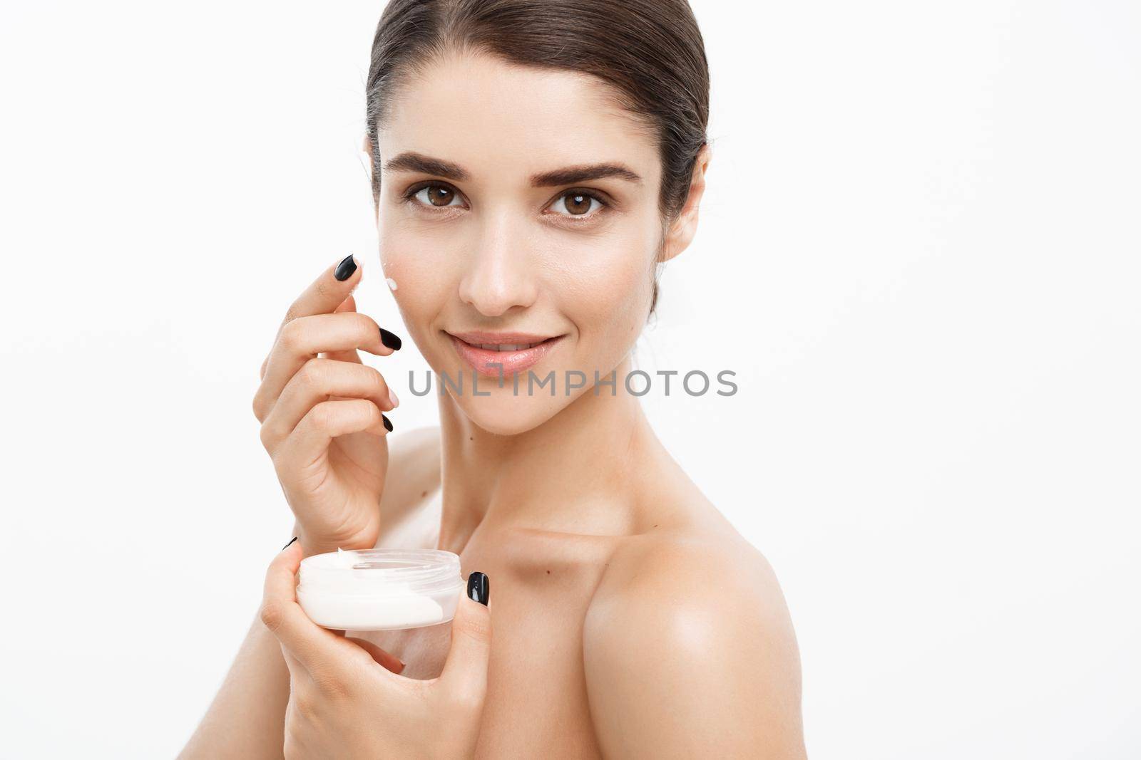 Beauty Youth Skin Care Concept - Close up Beautiful Caucasian Woman Face Portrait applying some cream to her face. Beautiful Spa model Girl with Perfect Fresh Clean Skin over white background. by Benzoix