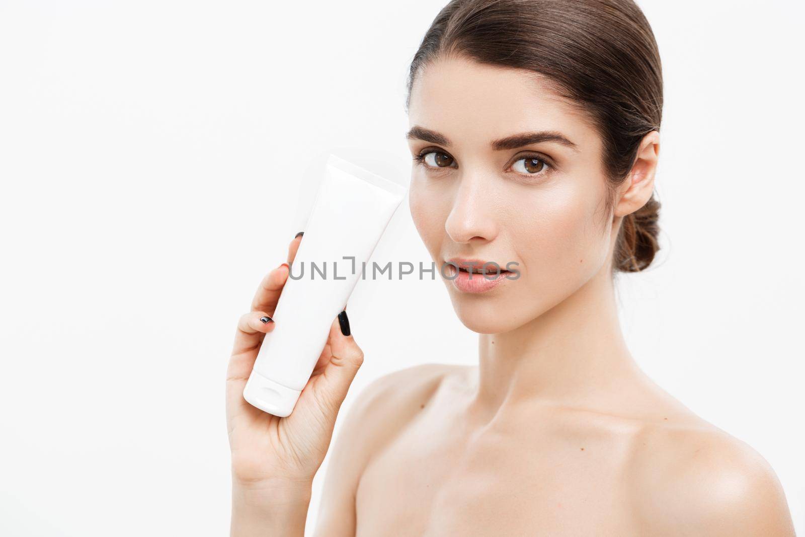 Beauty Youth Skin Care Concept - Beautiful Caucasian Woman Face Portrait holding and presenting cream tube product. Beautiful Spa model Girl with Perfect Fresh Clean Skin over white background