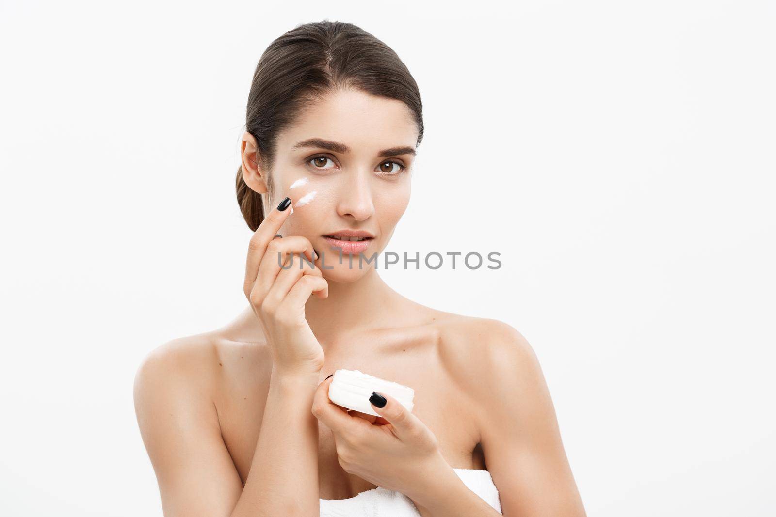 Beauty Youth Skin Care Concept - Close up Beautiful Caucasian Woman Face Portrait applying some cream to her face. Beautiful Spa model Girl with Perfect Fresh Clean Skin over white background. by Benzoix