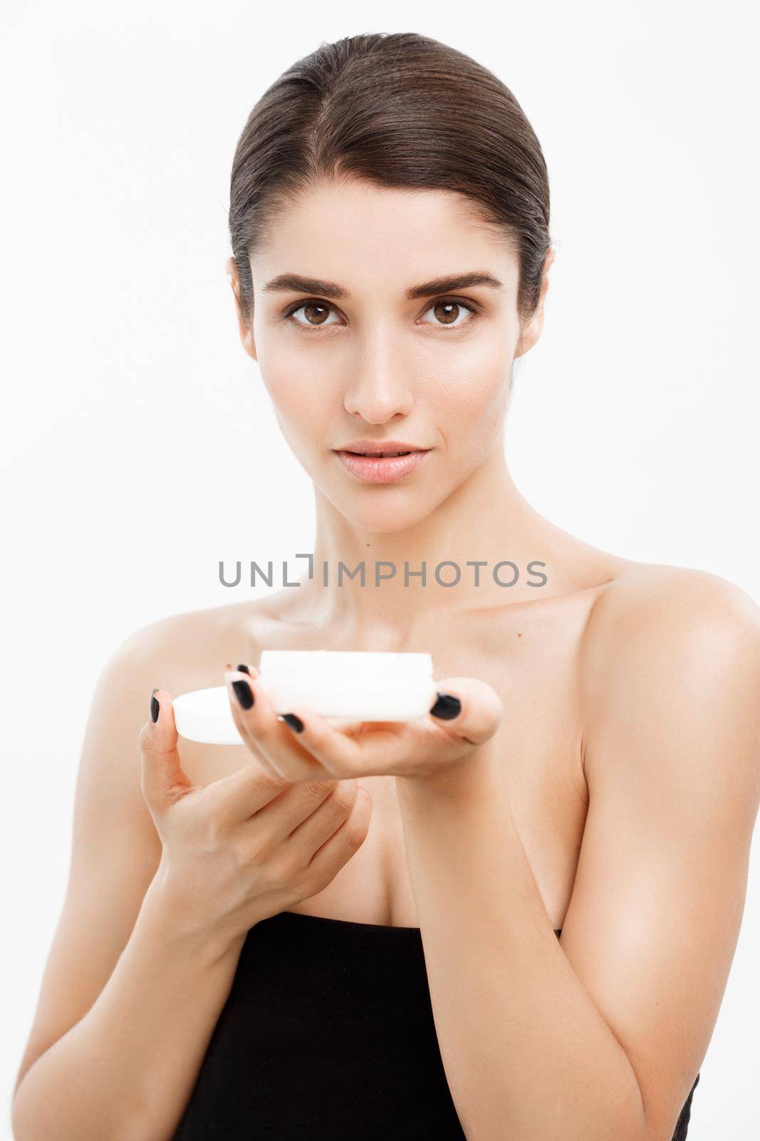Beauty Youth Skin Care Concept - Close up Beautiful Caucasian Woman Face Portrait presenting cream jar for skin care over white background. by Benzoix