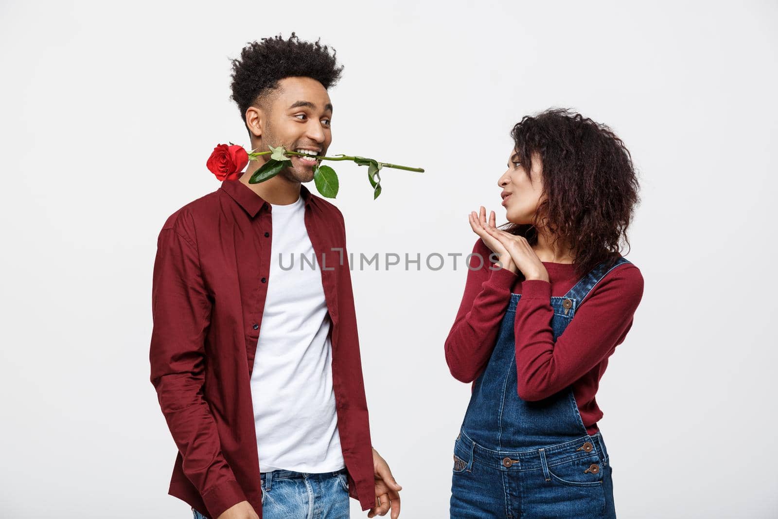 Romantic African American man in Love, holding a rose between his teeth standing in front of his girlfriend