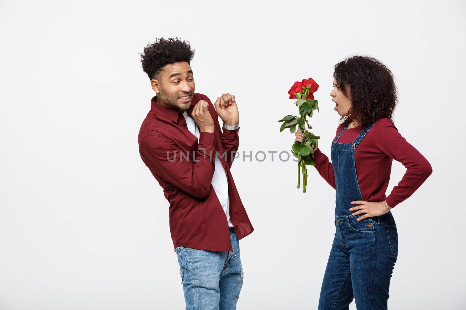 Portrait of a disappointed young woman holding red rose with while standing and angry on her boyfriend isolated over white background by Benzoix