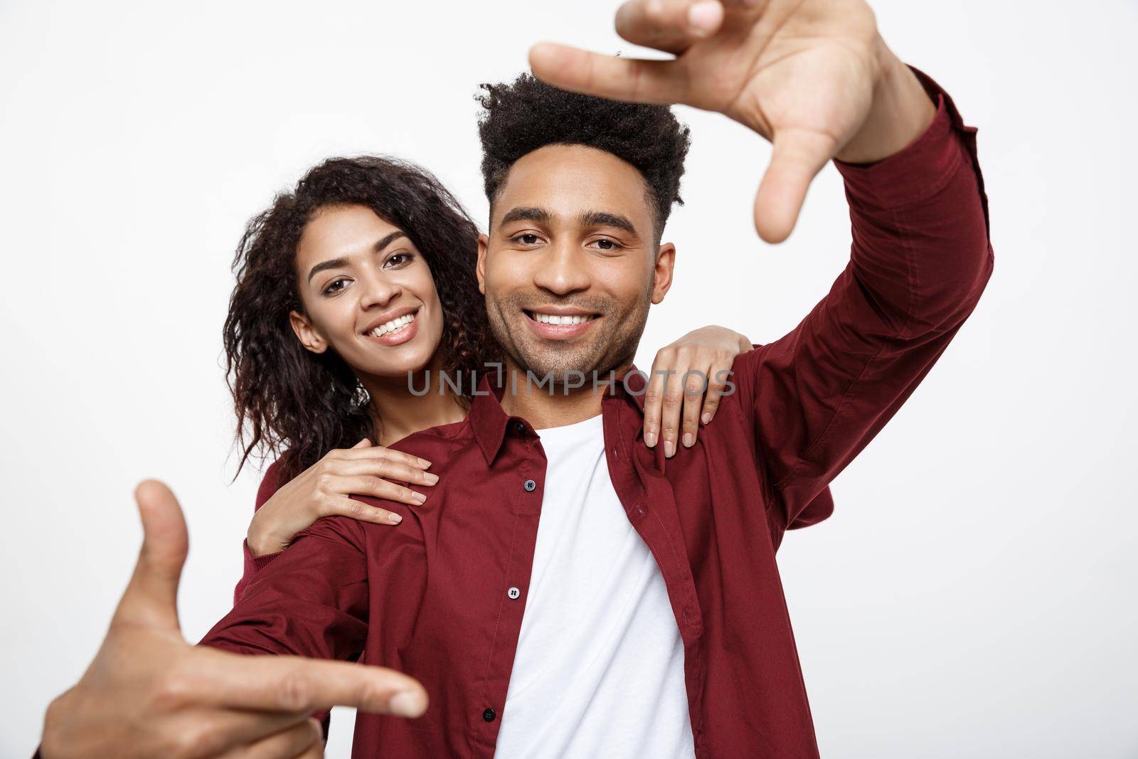 Happy young African American couple looking through a finger frame and smiling while standing isolated on white