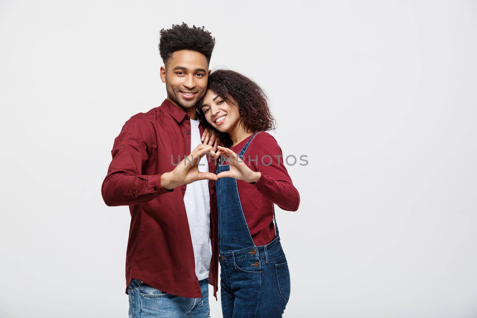 Portrait of a smiling young african couple dressed in casual clothes hugging and showing heart gesture with fingers isolated over white background by Benzoix