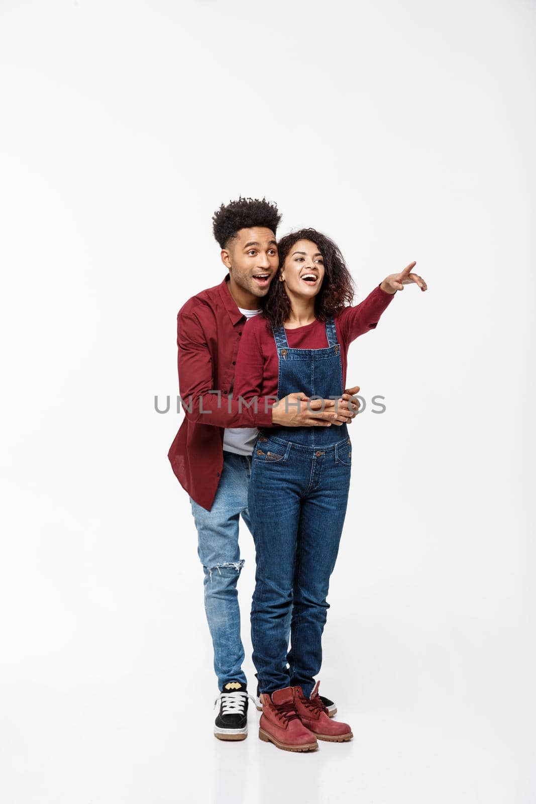 full length of smiling African American boyfriend and girlfriend pointing away isolated on white background