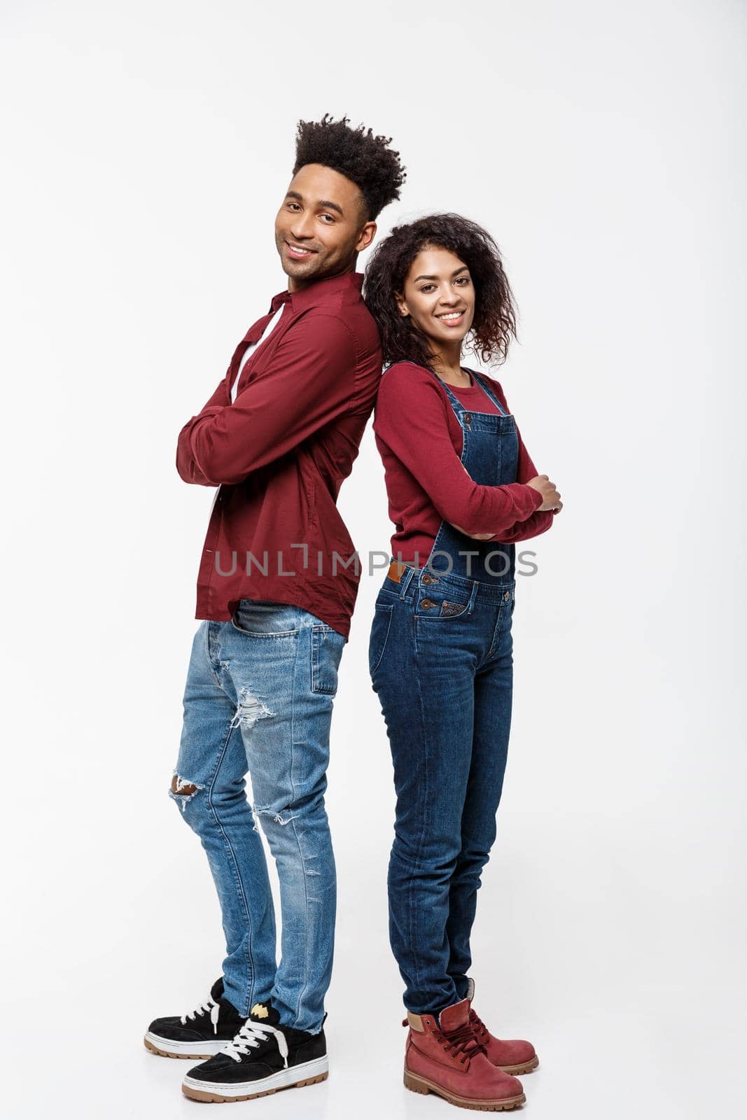 Cheerful African American man and woman with crossed hands standing back to back over isolated white background