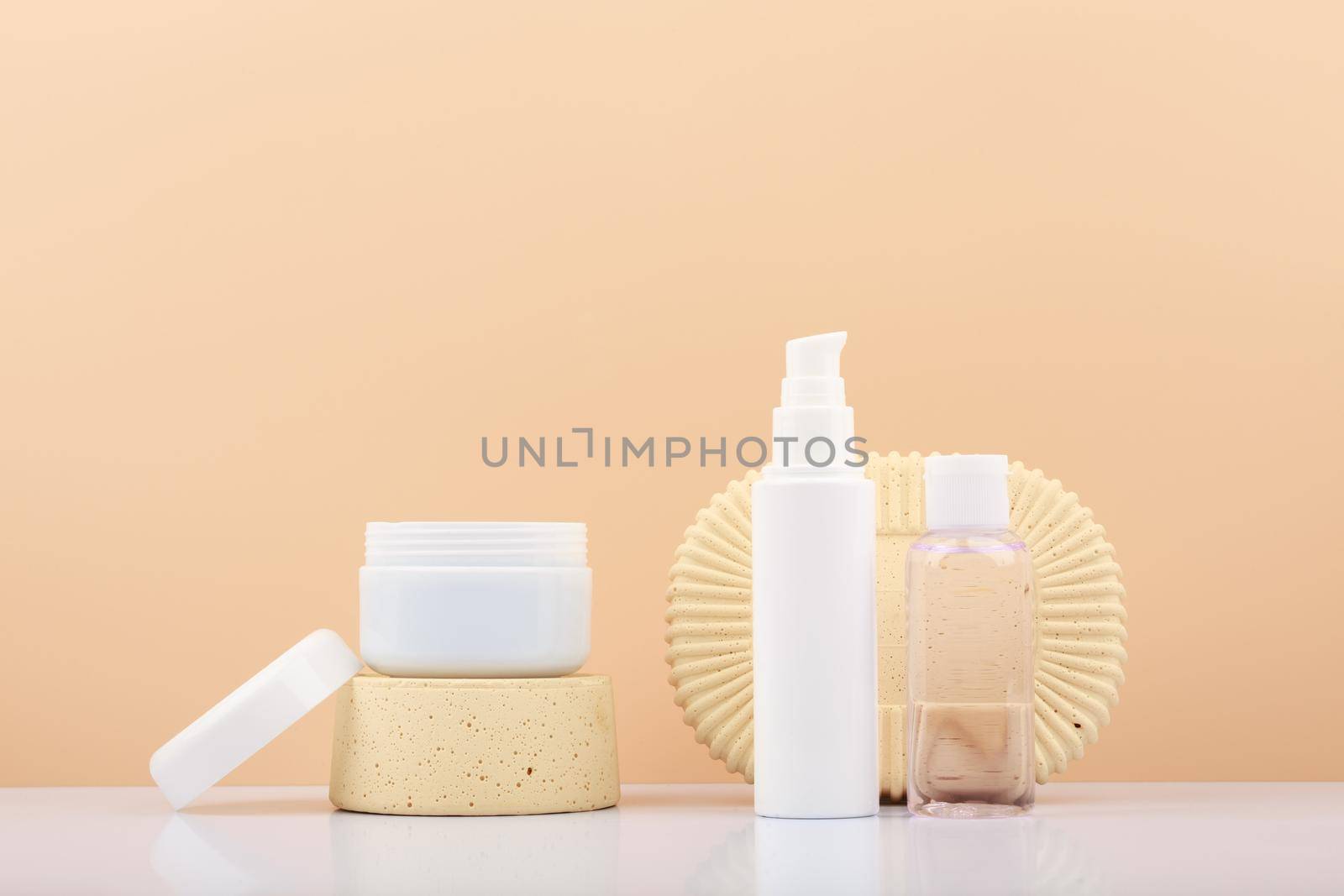 Opened cream jar on podium and tubes with cosmetic products for skin care against beige background by Senorina_Irina