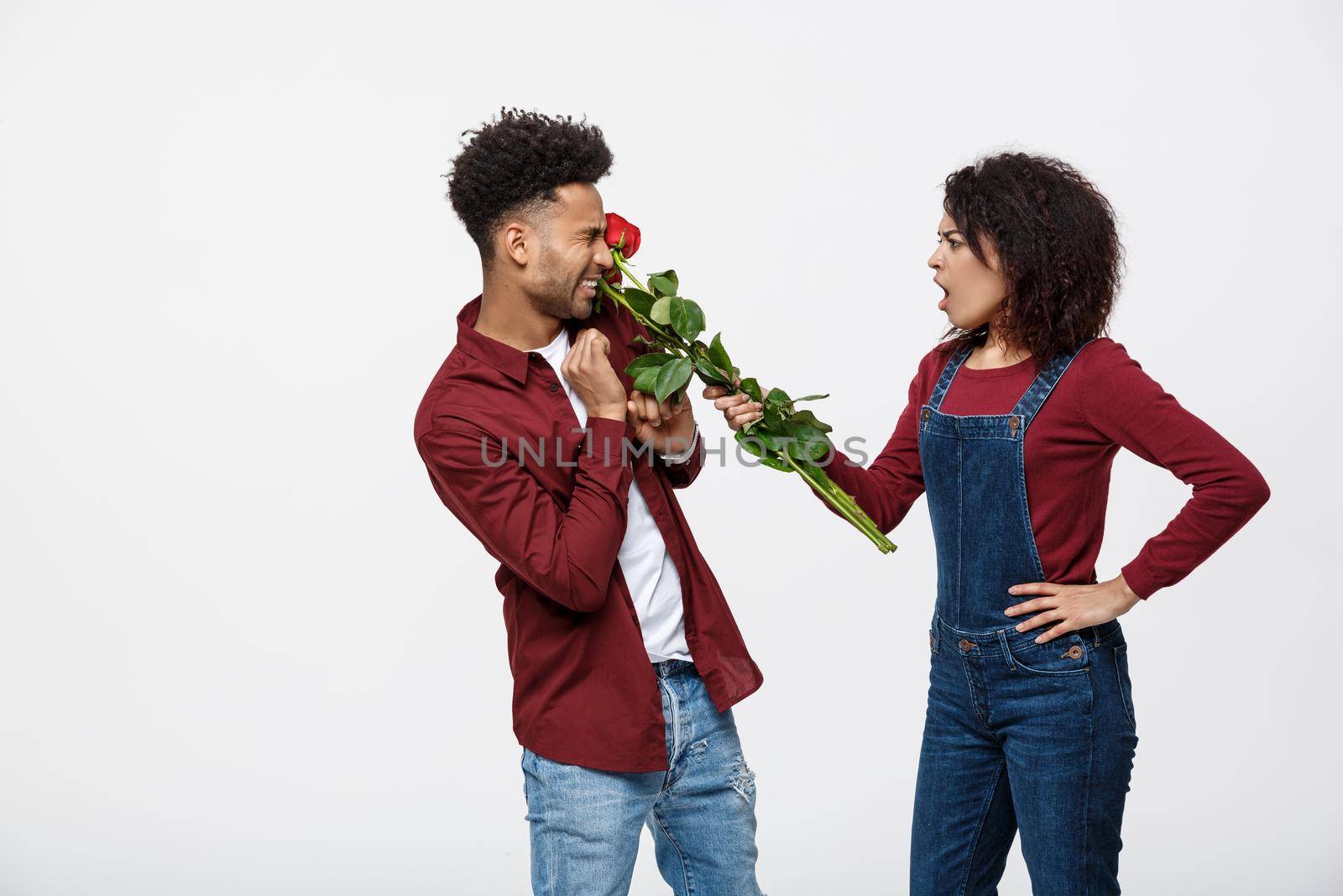 Portrait of a disappointed young woman holding red rose with while standing and angry on her boyfriend isolated over white background by Benzoix