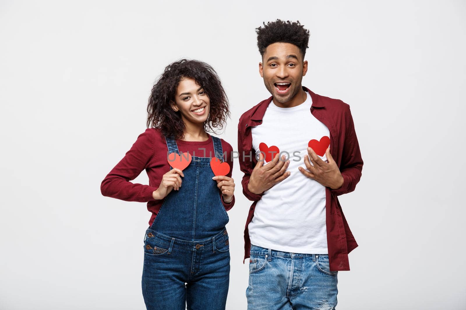 Portrait of african american cheerful couple holding red paper heart enjoy playing standing over grey background.