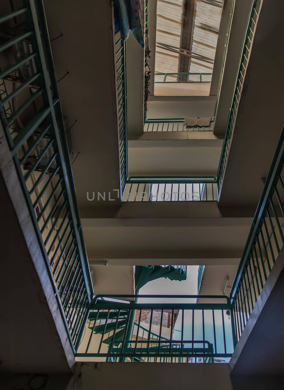 Bangkok, Thailand - 25 Jan 2020 : Looking up from under view upstairs walkway of an old apartment building with green metal rails and skylight. Selective focus.