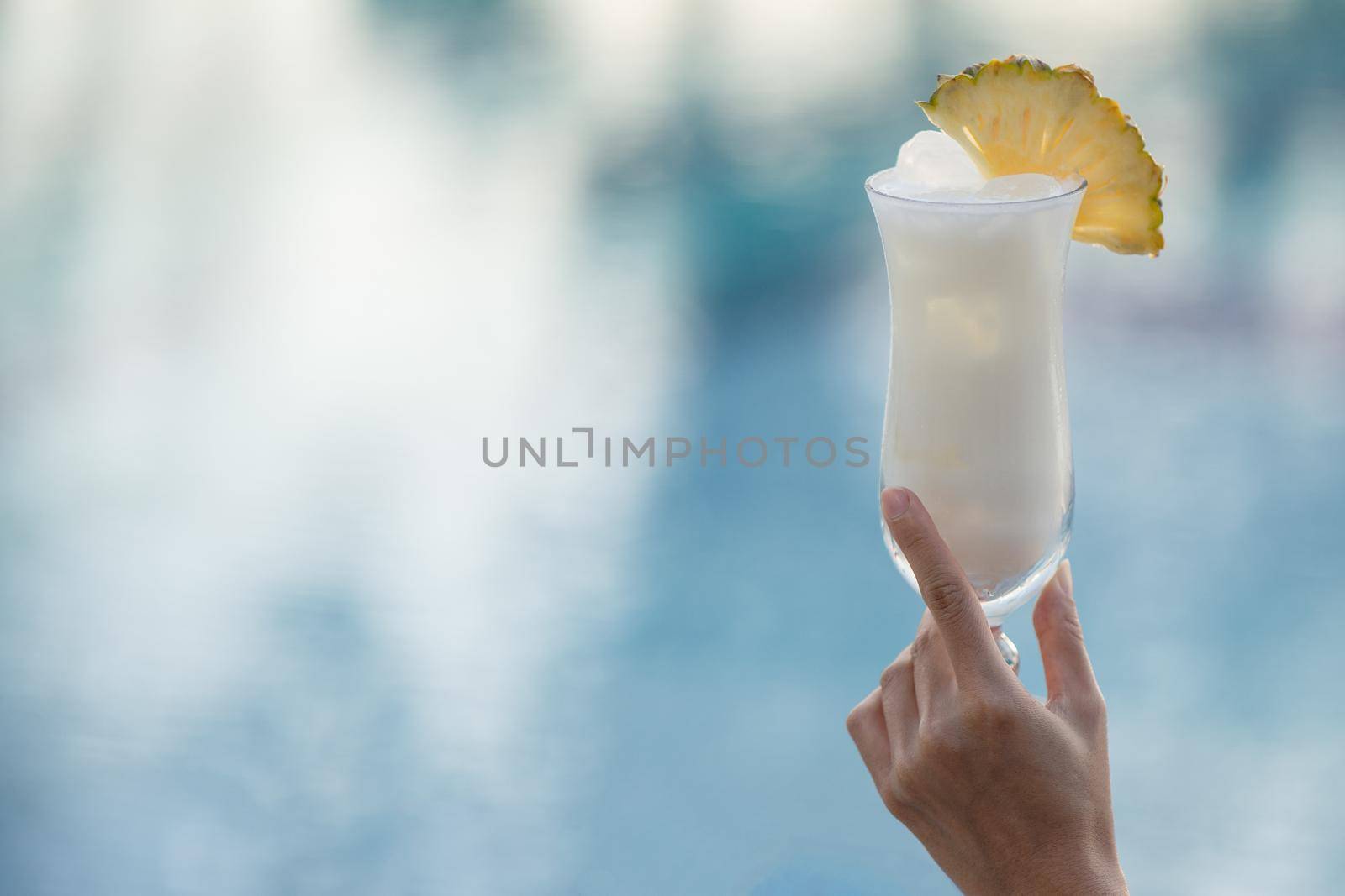 Woman hand holding a glass of cocktail on the edge of the pool.