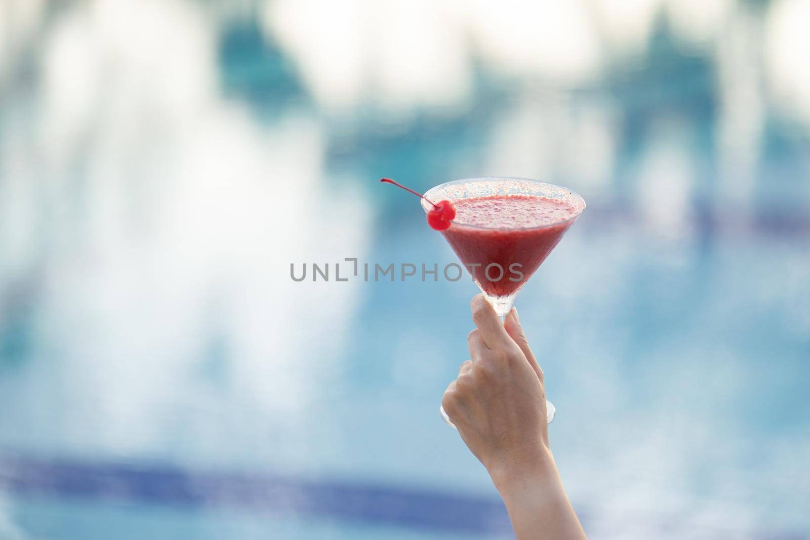 Woman hand holding a glass of cocktail on the edge of the pool.