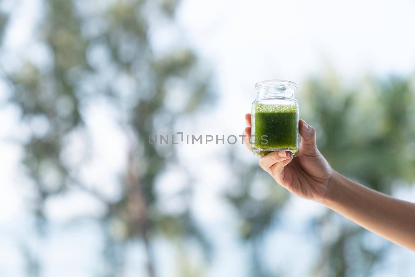 Woman hand holding a green smoothies on garden background. Healthy smoothies.