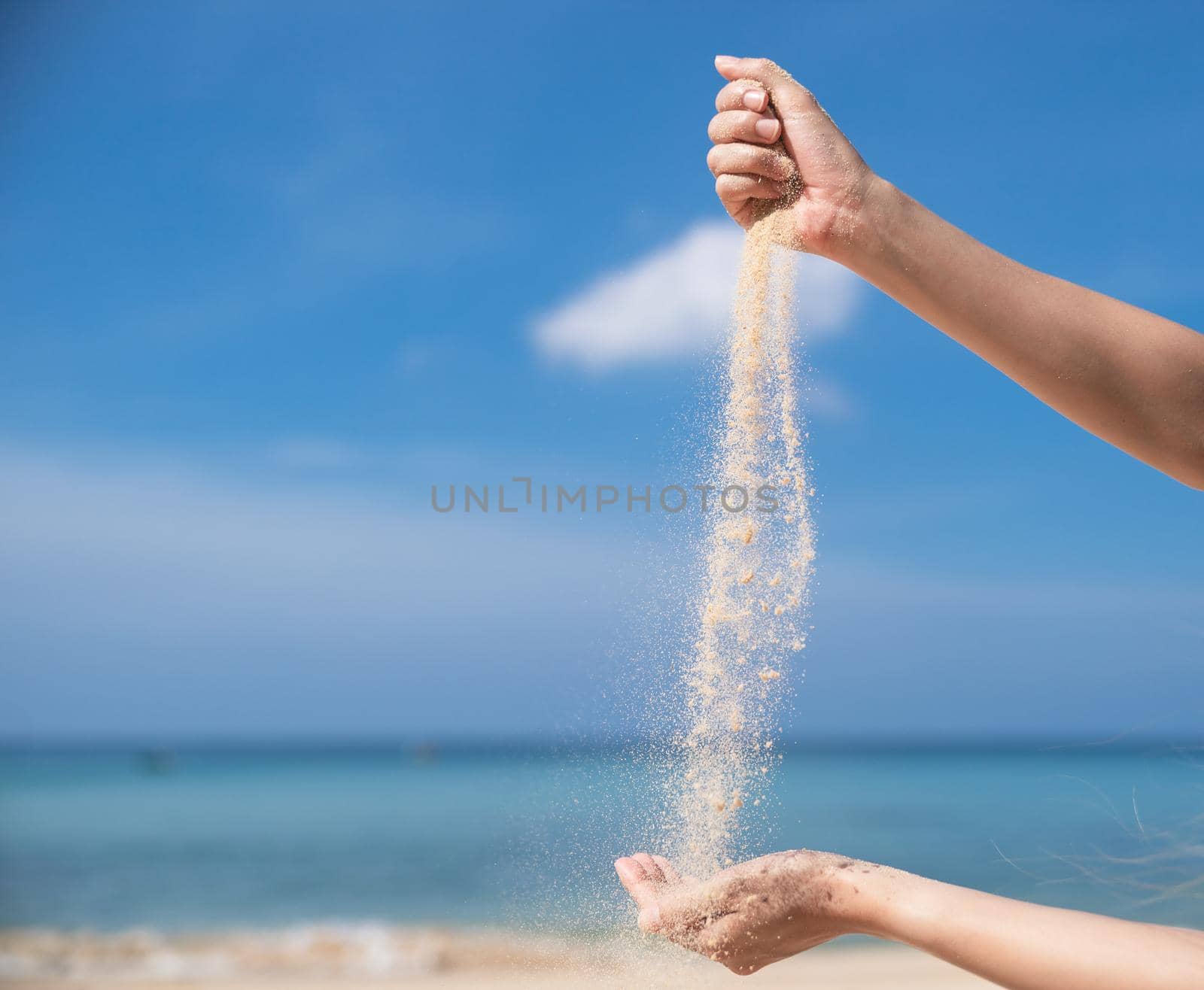 Woman pouring the sand from hand to hand on the beach, blue sky. by sirawit99