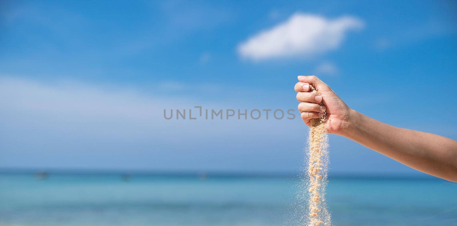 Woman pouring the sand from hand on the beach, blue sky.
