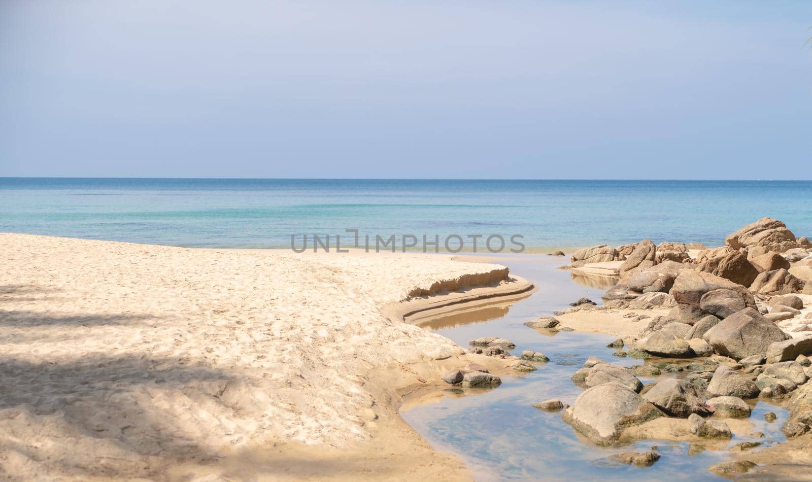 Sea, sand beach with rocks and blue sky.