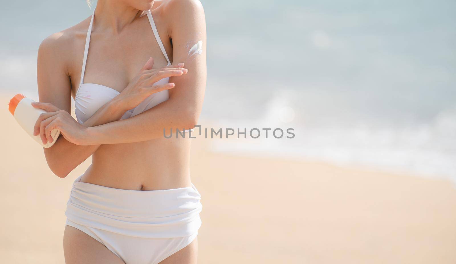 Woman applying Sunscreen in her body on the beach. by sirawit99