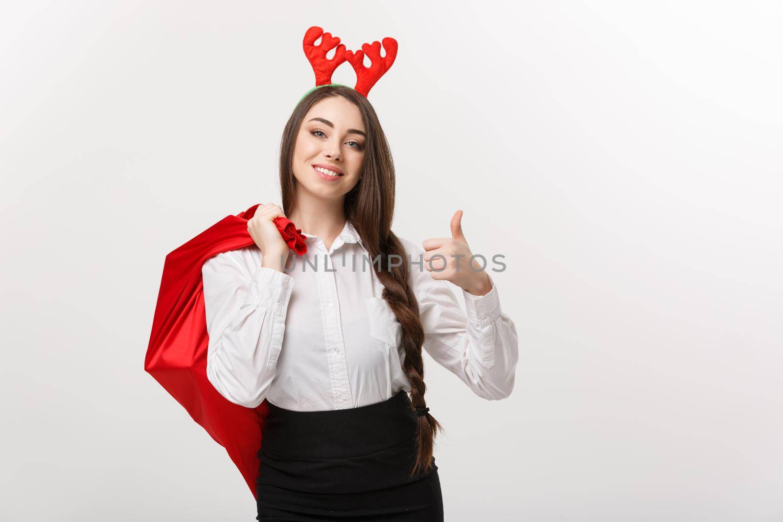 Christmas Concept - Young beautiful business woman in christmas theme holding santa red bag giving thumb up.