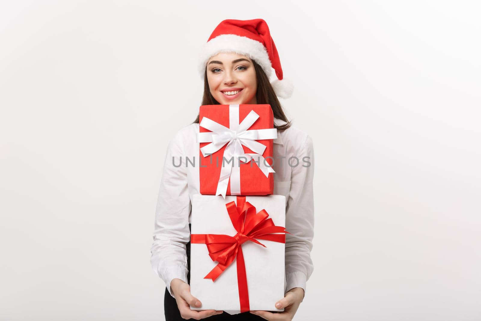 Business Concept - Beautiful young caucasian business woman with santa hat holding a lot of christmas gift boxes with copy space on side.