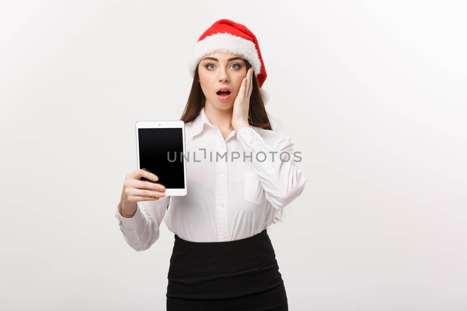 Business Concept - young caucasian business woman in Christmas theme showing digital tablet with surprising facial expression.