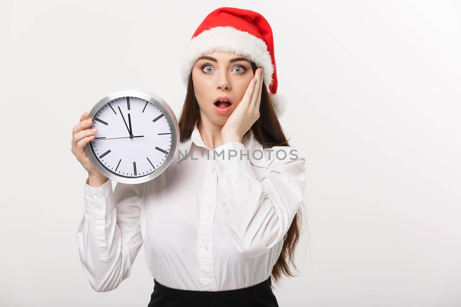 Time management concept - Young business woman with santa hat holding a clock isolated over white background. by Benzoix