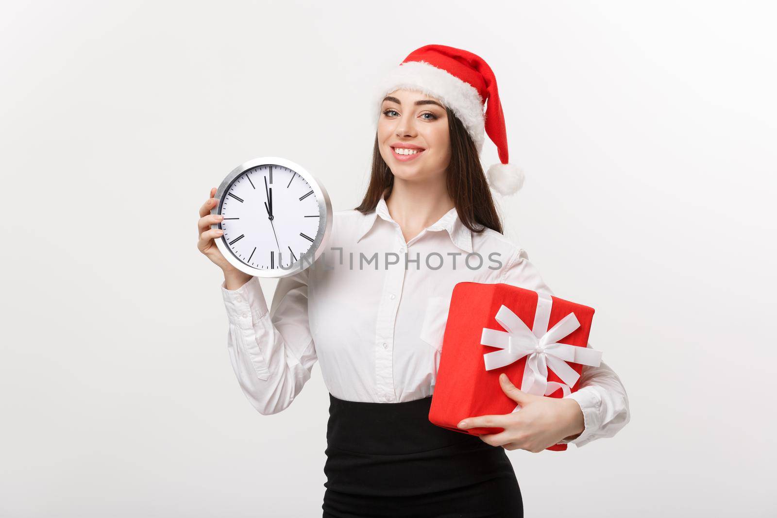 Time management concept - Young business woman with santa hat holding a clock and present isolated over white background. by Benzoix