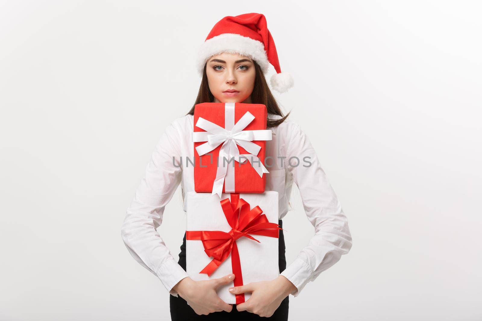 Business Concept - Beautiful young caucasian business woman with santa hat holding a lot of gift boxes with worry facial expression. by Benzoix