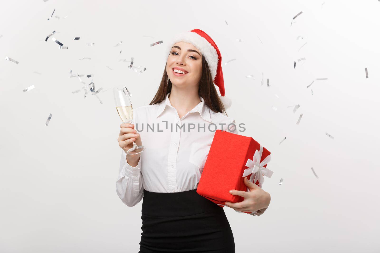 Christmas Concept - young business woman holding champagne and present with confetti background. by Benzoix