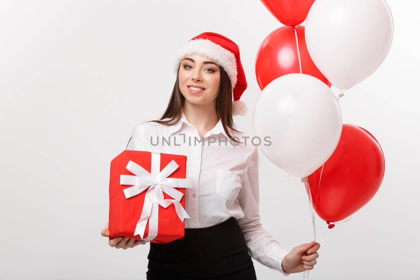 Christmas Concept - young happy caucasian business woman with santa hat holding gift box and balloon with copy space on side. by Benzoix