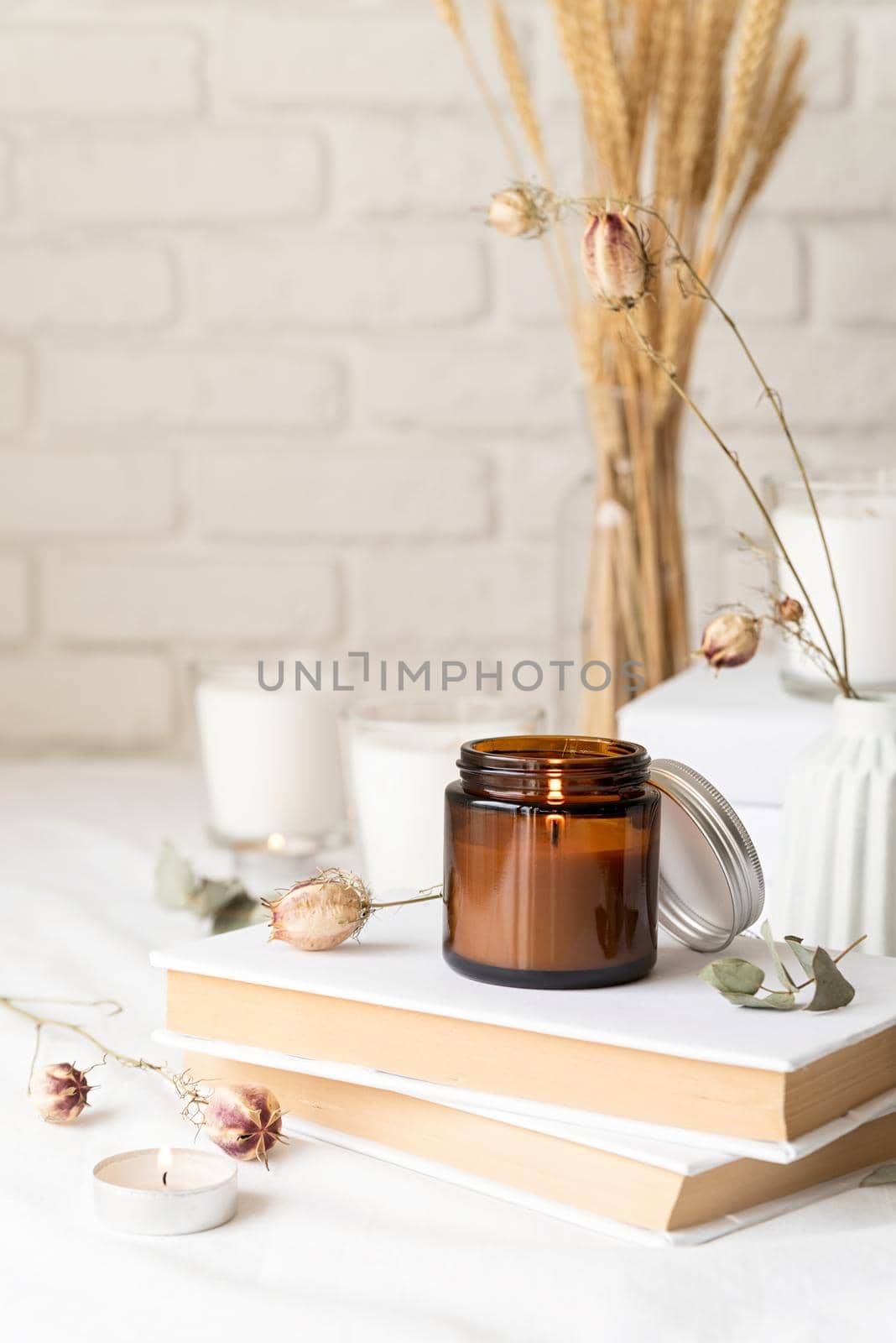 Home decoration and interior. Beautiful burning candles with eucalyptus leaves and dry flowers on pile of white books