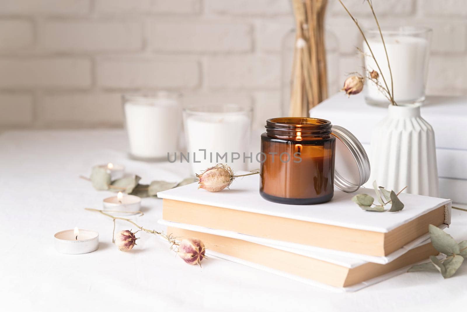 Beautiful burning candles with eucalyptus leaves and dry flowers on pile of white books by Desperada