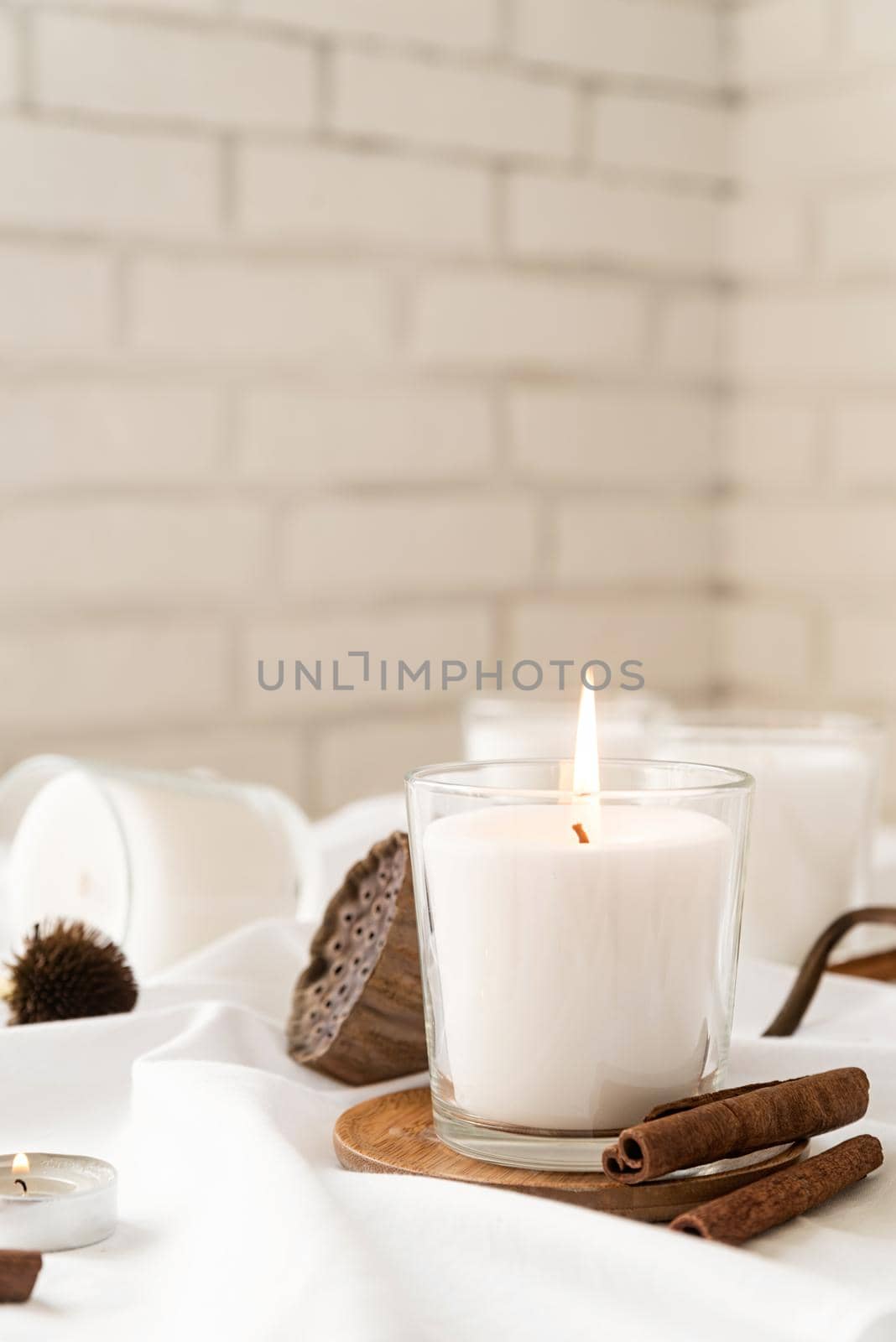 Home decoration and interior. Beautiful burning candles with cinnamon and dry flowers on white fabric background