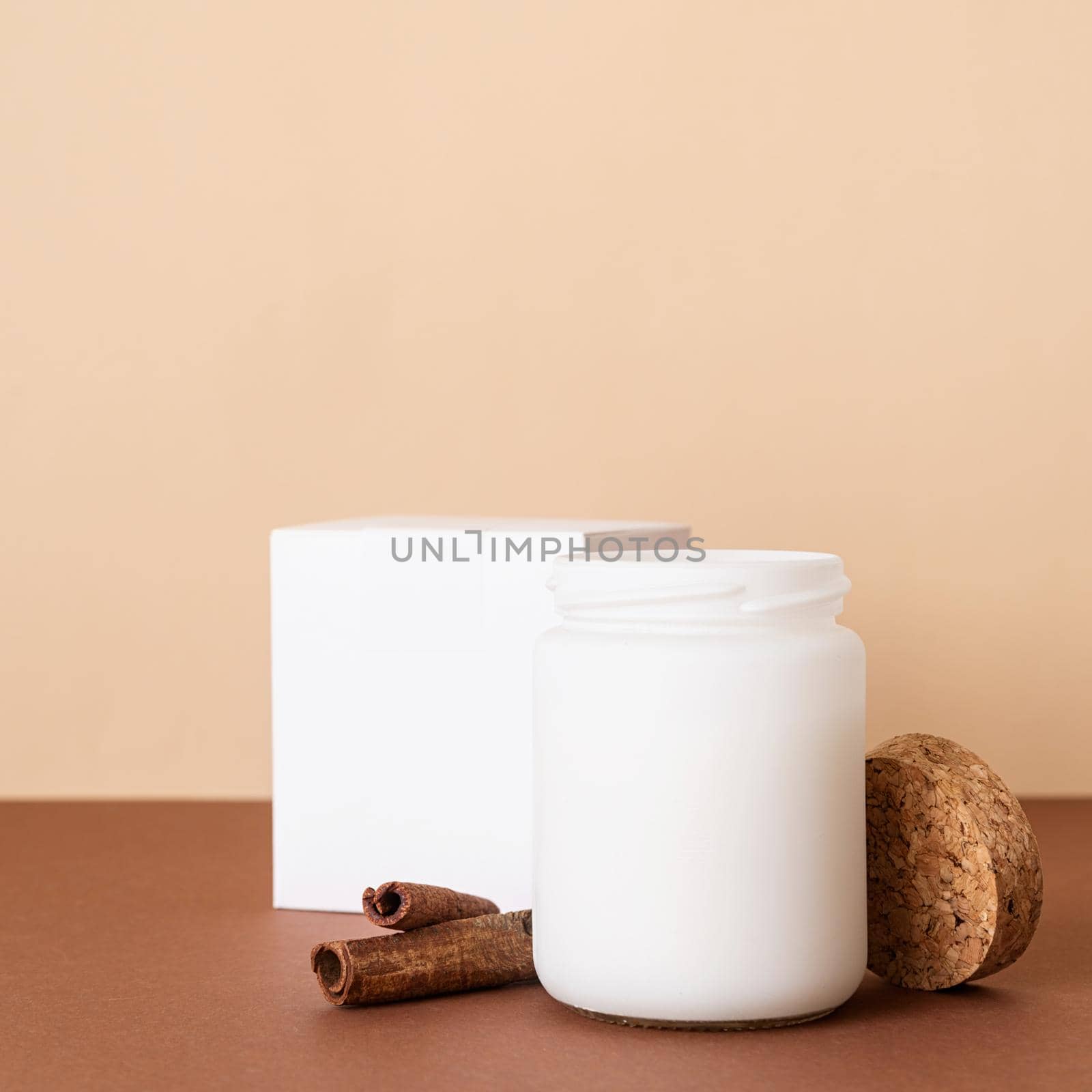 Home decoration and interior. Beautiful white candle with cinnamon sticks on brown solid background