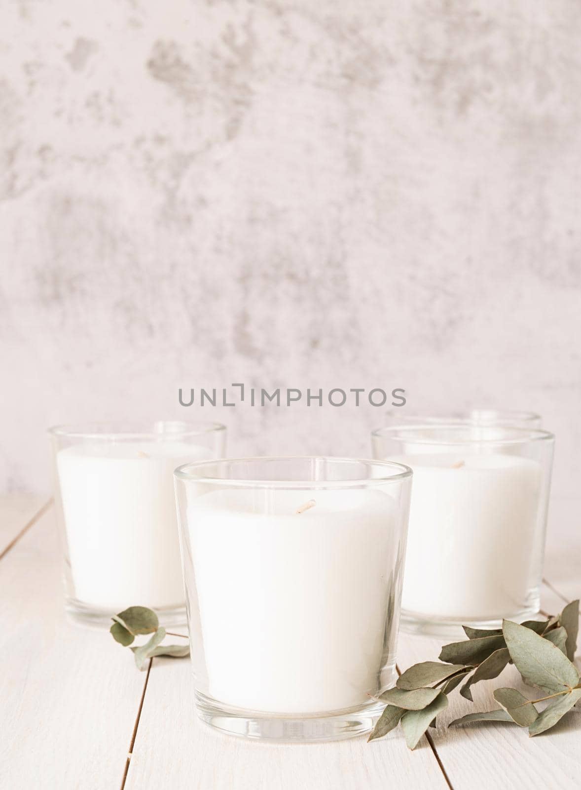 Home decoration and interior. Beautiful white burning candles with eucalyptus leaves on white wooden background