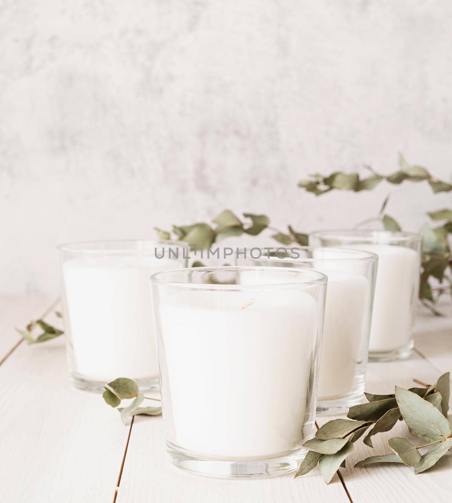 Home decoration and interior. Beautiful white burning candles with eucalyptus leaves on white wooden background