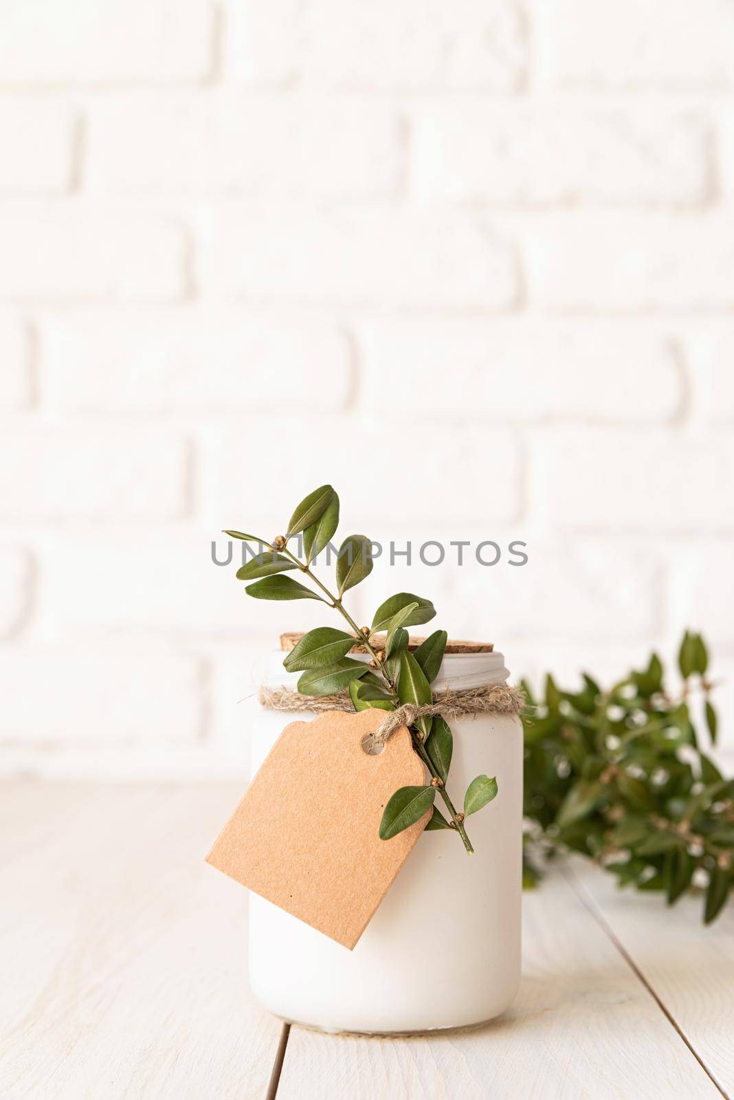 Home decoration and interior. Beautiful white candle with fresh green leaves on white wooden background